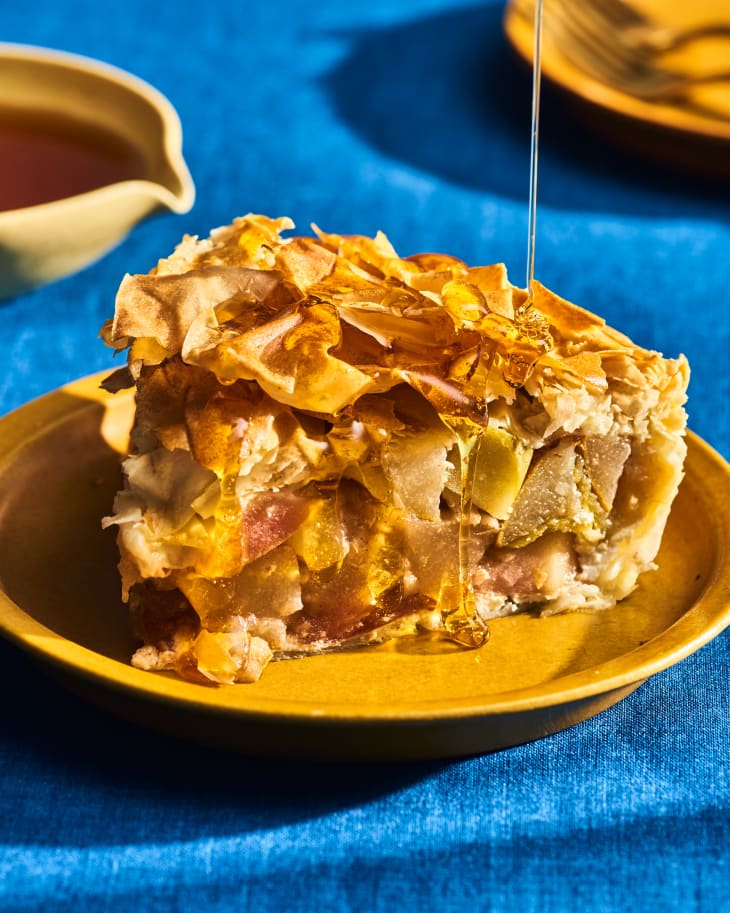 slice of pear apple pie on a yellow plate with honey being drizzled over the top. On thanksgiving table with blue tablecloth