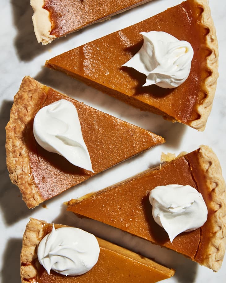 Pumpkin pie slices with whipped cream lined up on a marble counter