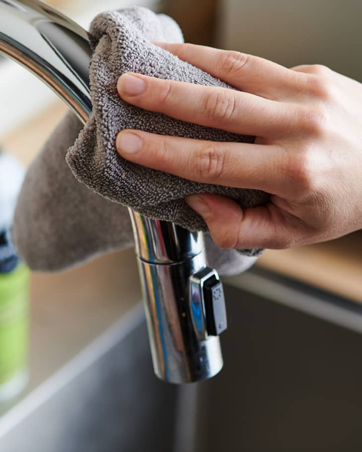 someone cleaning a kitchen sink faucet with a gray microfiber cloth