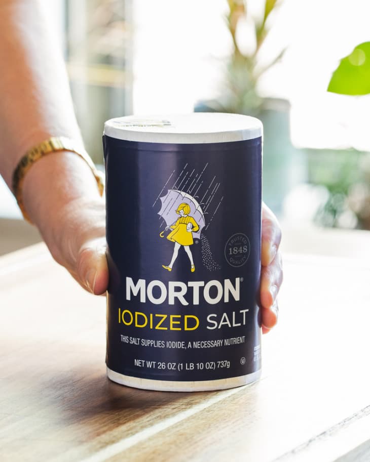 Someone holding a container of Morton Iodized table salt.