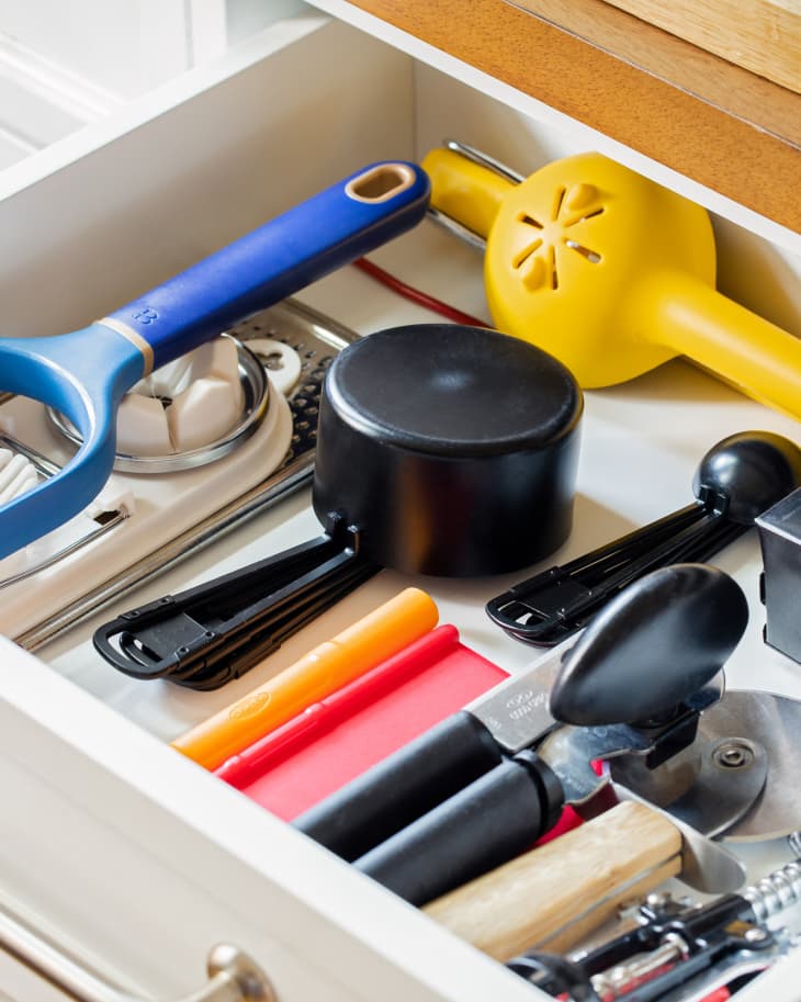 Organized kitchen drawer that full of tools like juicer, measuring cups, can opener, etc