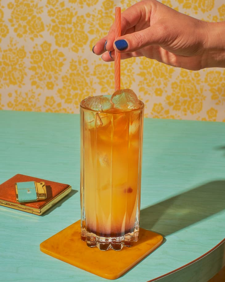 cocktail on blue surface on brown coaster with someone stirring