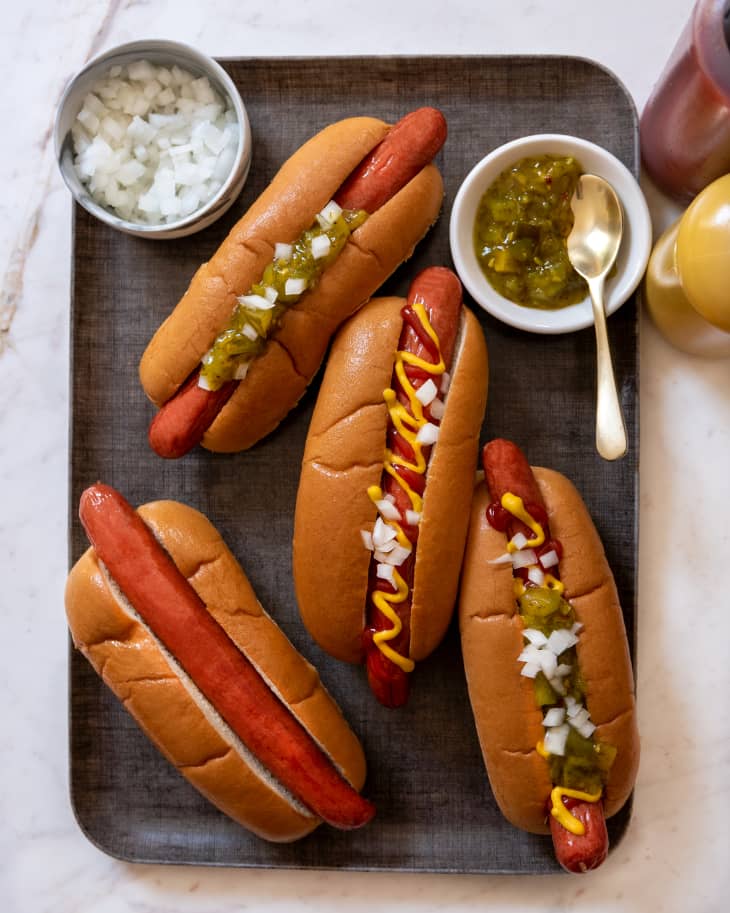 Four hot dogs on platter with condiments in bowls nearby