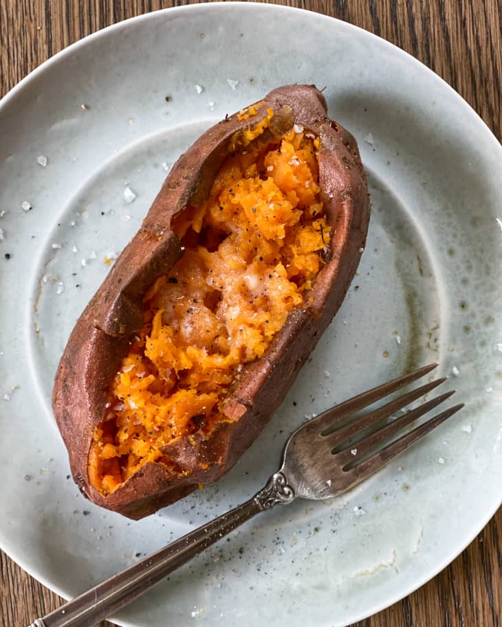 An air fryer sweet potato on a plate, with melted butter on top, and a fork sitting next to it on the plate.