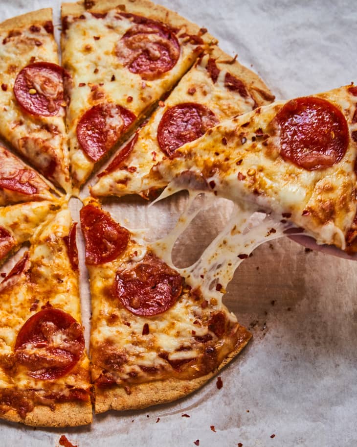 A whole pepperoni pizza with an Almond Flour Crust, cut into eight slices with one slice being lifted