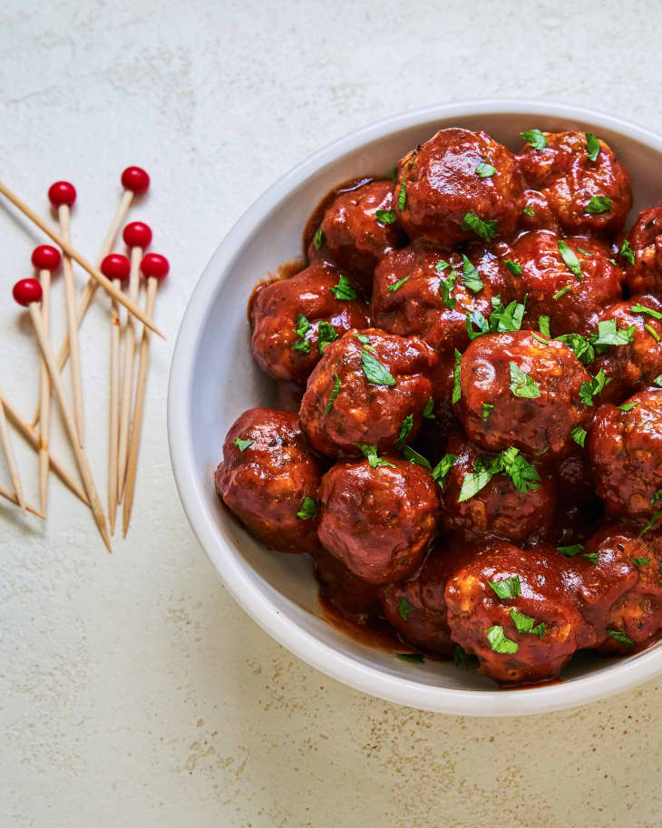 BBQ meatballs in a white bowl with toothpicks next to the bowl.
