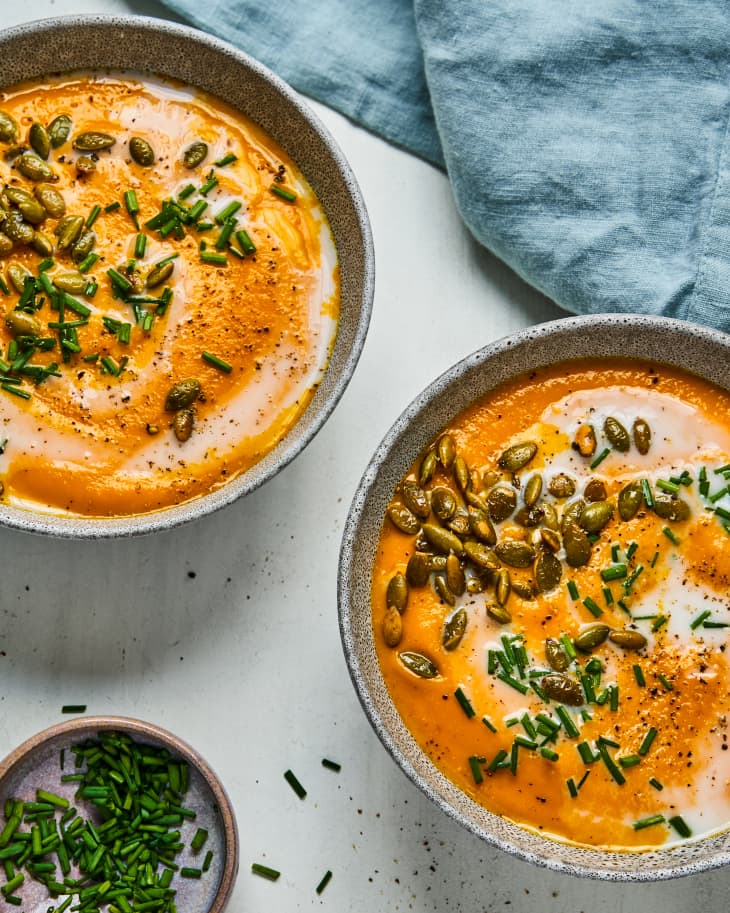 Two bowls of Carrot Ginger Soup with a cream and pine nut garnish