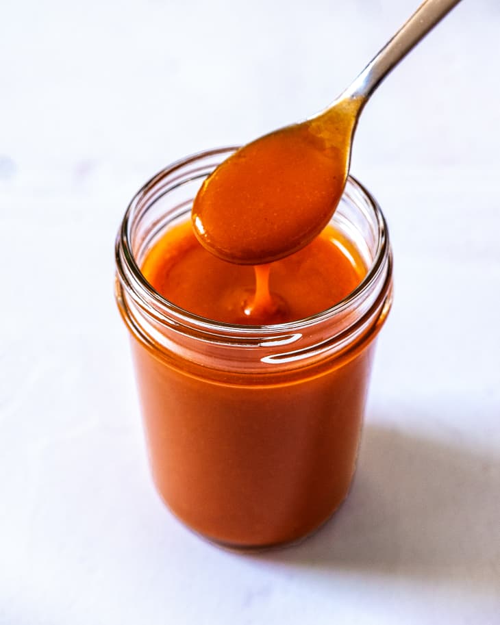 french dressing, which is reddish-orange in color, in a clear glass jar with a spoon being dipped into it