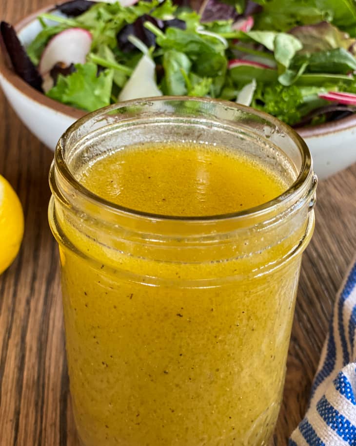 Lemon vinaigrette in a ball jar with a green salad in the background behind it.