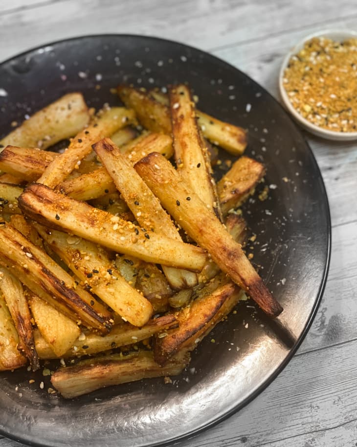 Roasted parsnips on a black plate with spices nearby