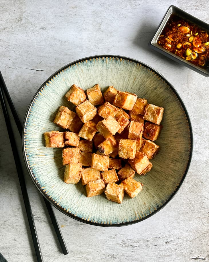 air fryer tofu in a bowl with chopsticks to the left and a bowl of scallion soy sauce