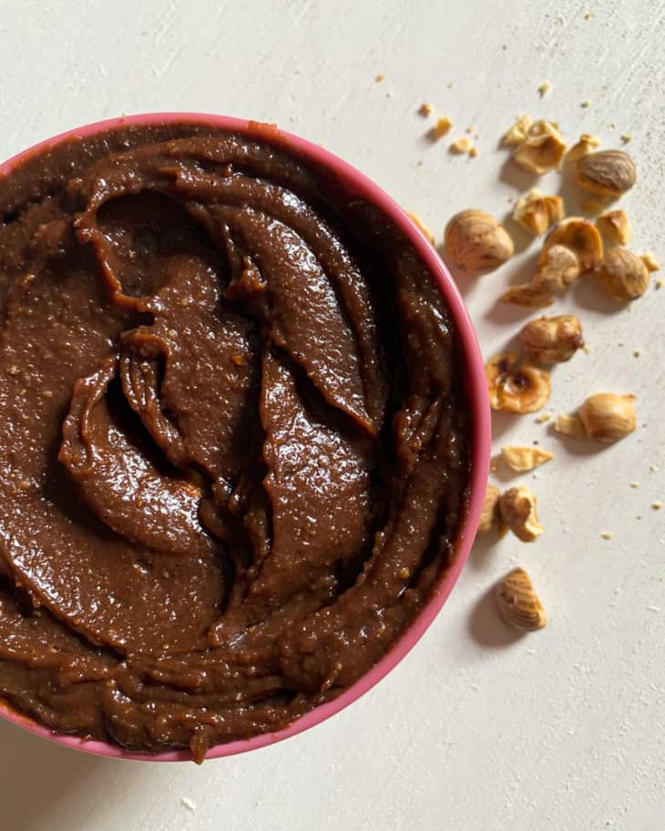 Homemade nutella in a pink bowl with hazelnuts in the background