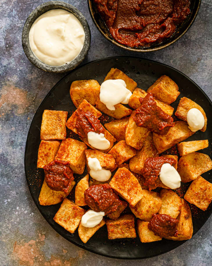 Patatas Bravas (chunks of fried potato) with red and white sauce, on a black plate