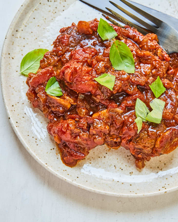 Steak Pizzaiola on a plate with red sauce and basil leaf garnish