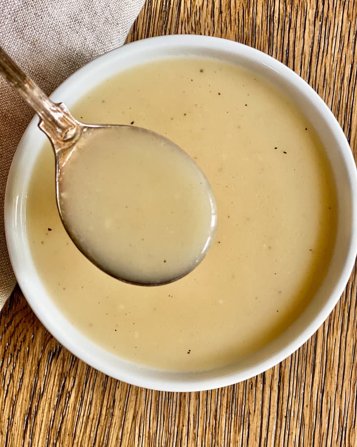 Veloute (a rich white sauce made with chicken, veal, pork, or fish stock, thickened with cream and egg yolks) in a white bowl, with a spoon picking up a spoonful of it