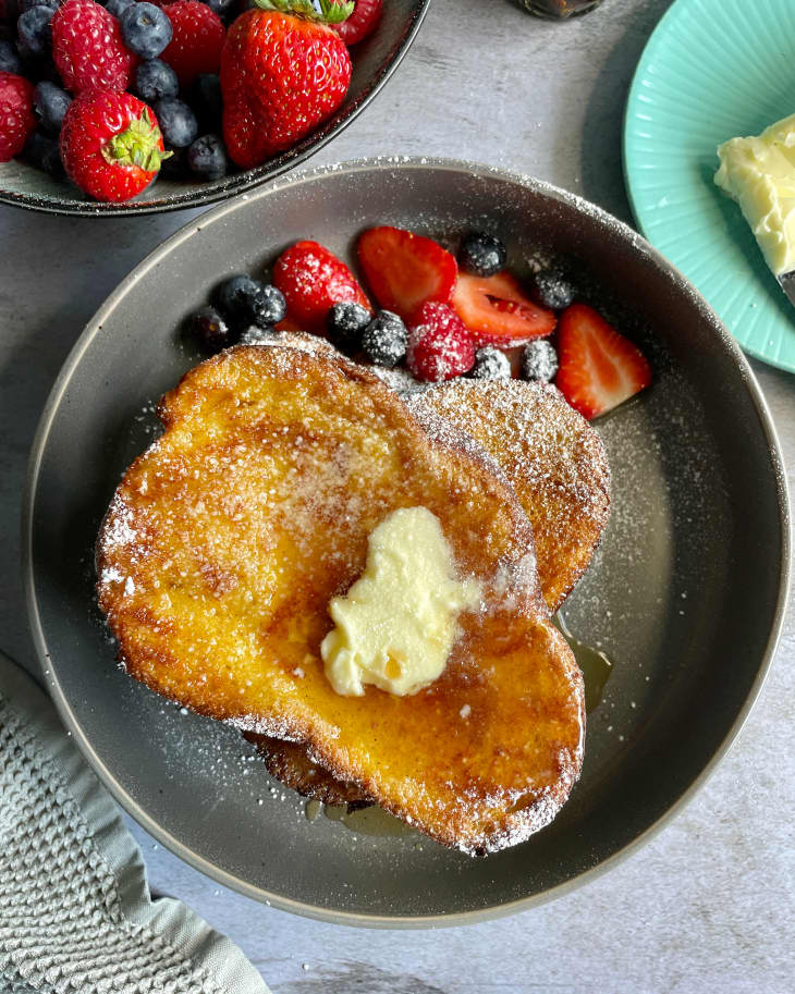 Air Fryer French Toast on a dark gray plate, with syrup and butter on top, and strawberries and blueberries on the side, photographed from the top looking down.