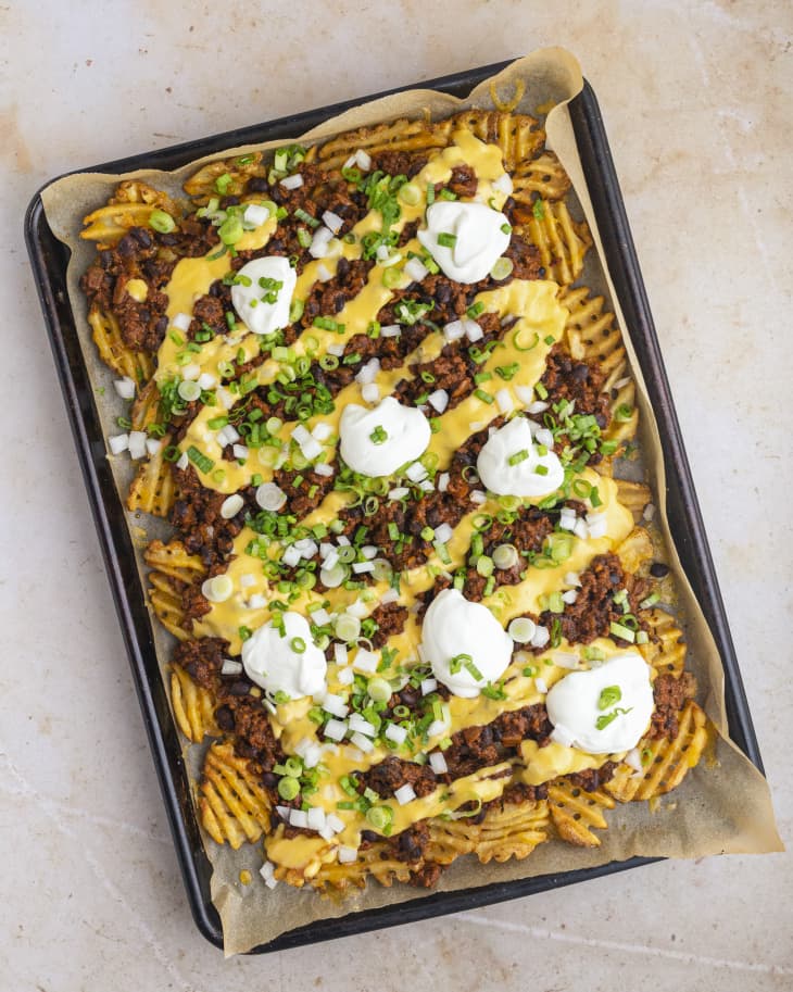 a tray of waffle fries with chili, melted cheese, sour cream, and onions.