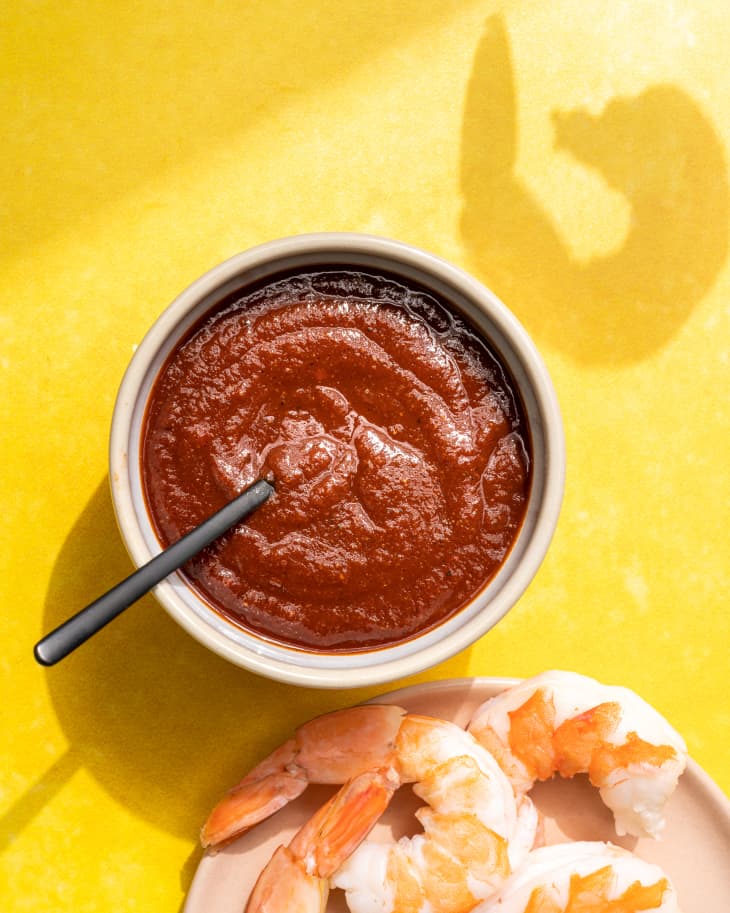 chili sauce in a bowl with a black spoon, on a yellow background, with a plate of shrimp on the side