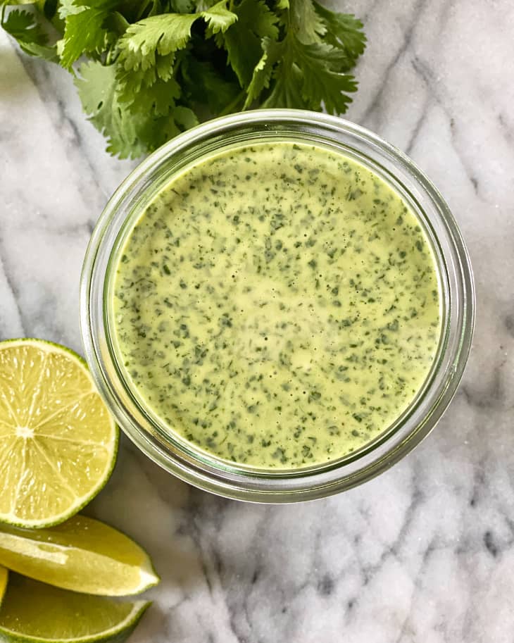 cilantro lime dressing in a glass jar, with whole cilantro and lime slices next to it