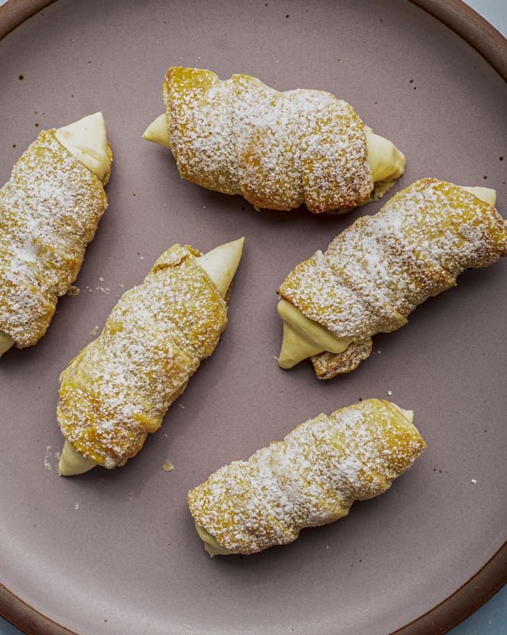 Cream horn pastries (croissant shaped pastry, filled with cream)  on a mauve plate, with  powdered sugar on top.
