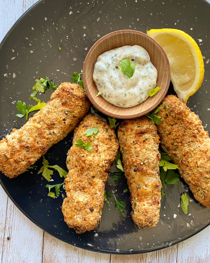 Fish sticks on a plate with tarter sauce and a lemon wedge.