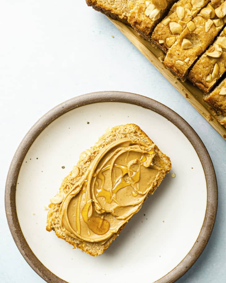 A slice of peanut butter bread with peanut butter and honey with the rest of the loaf sliced on a cutting board next to it