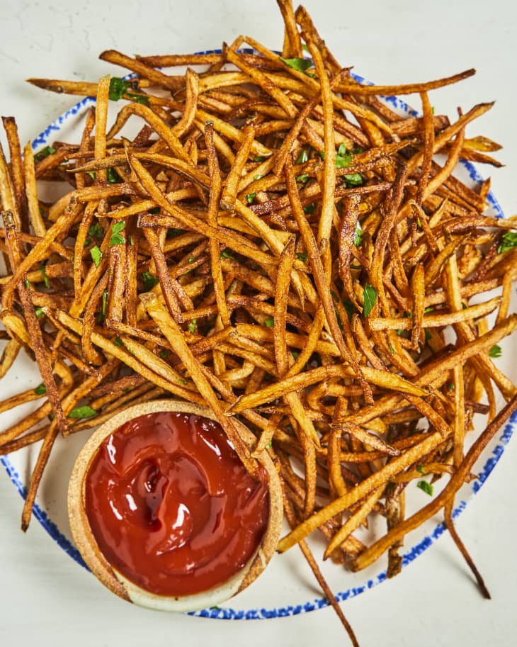 a pile of shoestring fries on a plate with ketchup