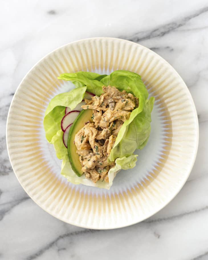 turkey salad made with leftover turkey, wrapped in a lettuce leaf, with sliced radishes, on a ceramic plate, on a marble countertop.