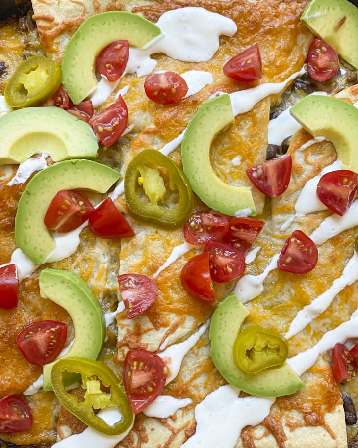 a burrito casserole with tomatoes, sliced avocado, jalepeno and sour cream on top.