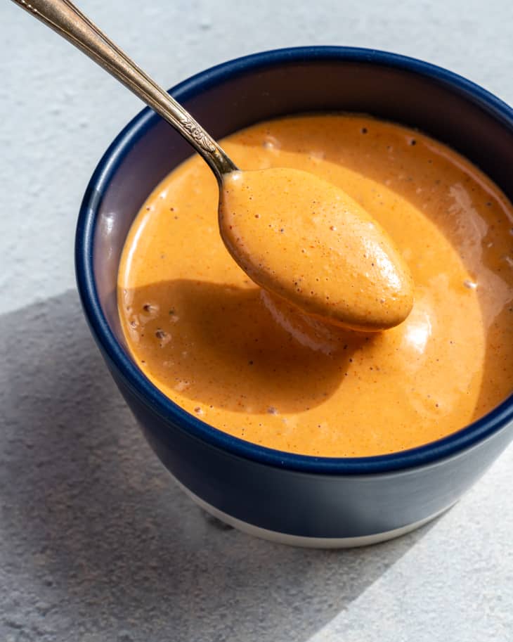 comeback sauce (southern mayo, ketchup and hot sauce based dressing)  in a small black bowl with a spoon taking a spoonful out.