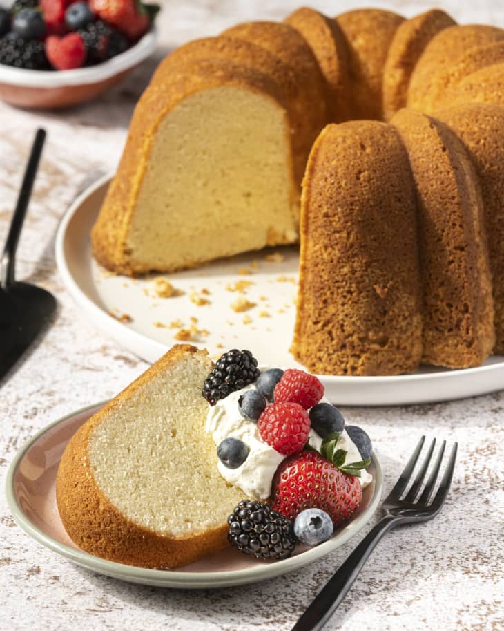 Cream cheese pound cake seen from the side, with one slice cut out with whipped cream and berries on it.