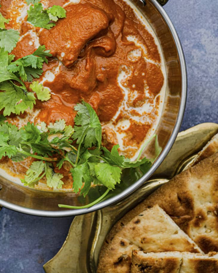 Butter chicken in a silver pot with parsley on top and fresh naan on the side.