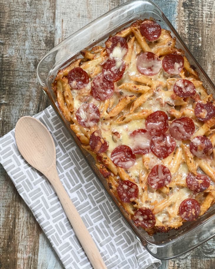 pepperoni pizza casserole in a glass baking tray with a wooden spoon on the side.