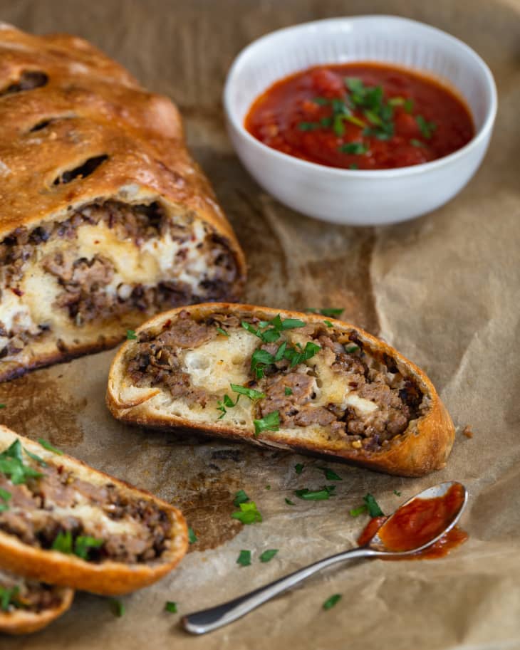 slices of sausage bread sliced off of the full roll, on brown wrapping paper, with a side of marinara sauce in a white bowl and a silver spoon with some sauce on it in the foreground.