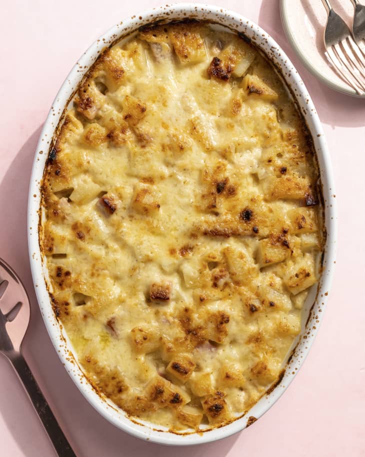 ham and potato casserole in an oval serving dish on a pink background