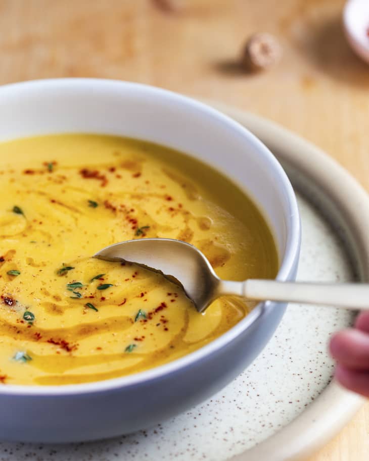 A pureed acorn squash soup in a white ceramic bowl with red spices sprinkled on top