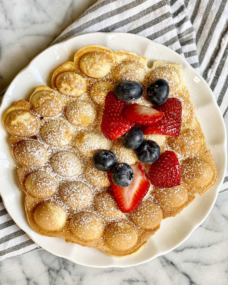 Bubble waffles on a plate with powdered sugar and fruit and whipped cream topping