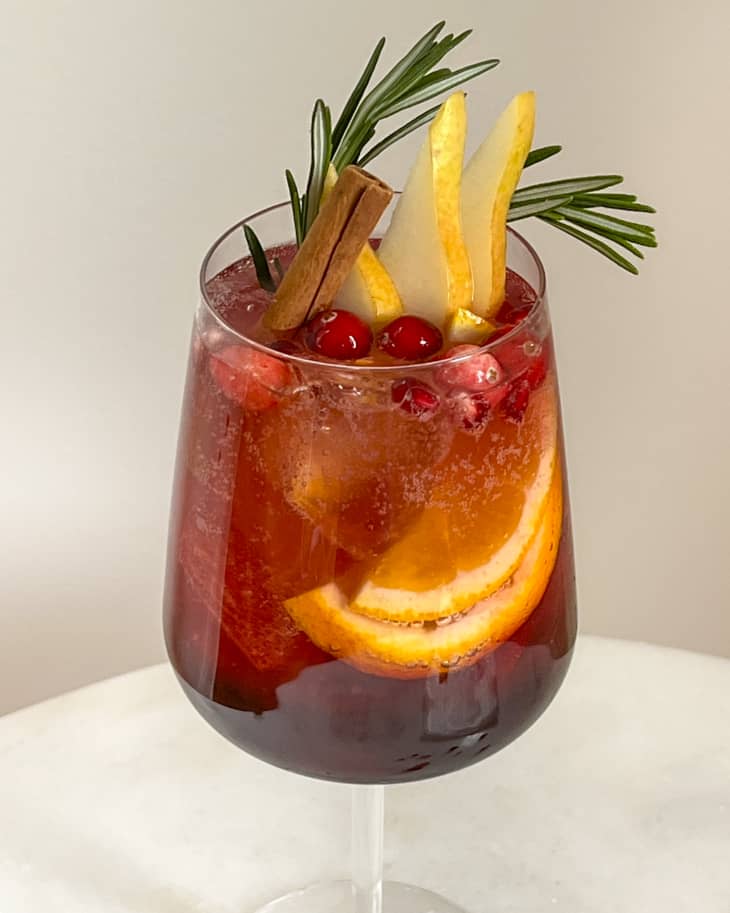 Holiday sangria garnished with a pine sprig, pear slices, cranberries and oranges in a wine glass