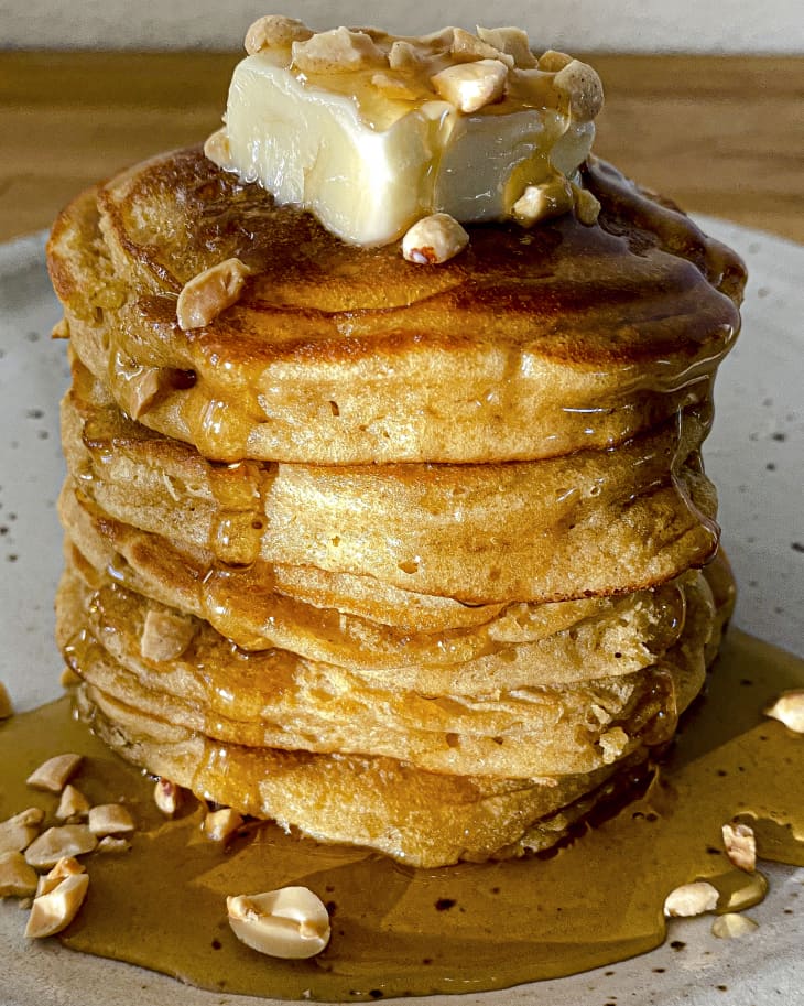 Peanut butter pancakes on a plate with syrup poured over it and nuts on top