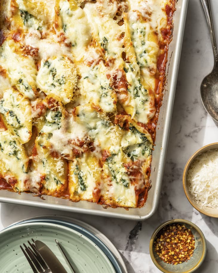 Spinach stuffed shells in a baking tin, with side plates and spices on the side