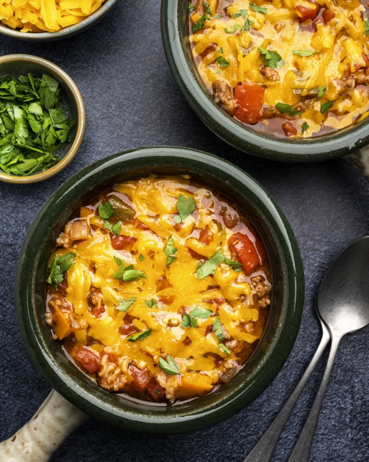 Stuffed pepper soup in a bowl with melted cheese and garnishes in small bowls on the side