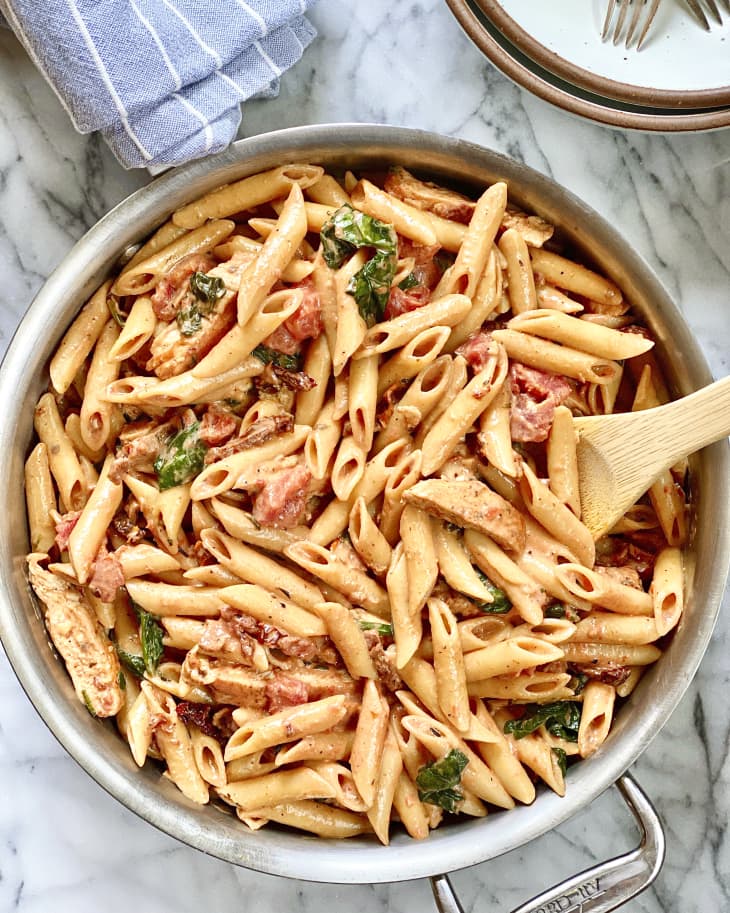 Tuscan chicken pasta  made with penne pasta in a bowl with a wooden spoon.