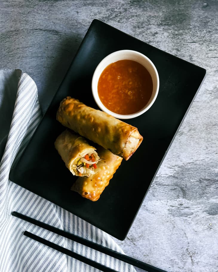 egg rolls on a rectangular black plate, with a red dipping sauce in a white ramekin on the side