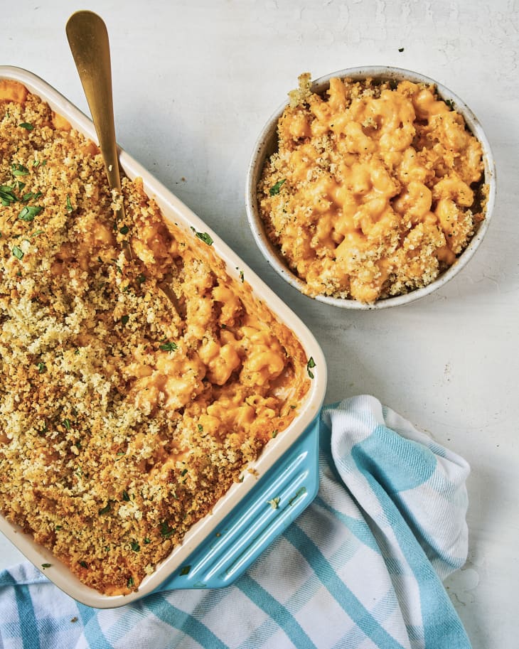 Buffalo Mac and cheese with a breadcrumb topping, in a white ceramic baking dish, with a turquoise handle, with a bowl of it on the side and a turquoise and white checkered dish closth under the baking dish.
