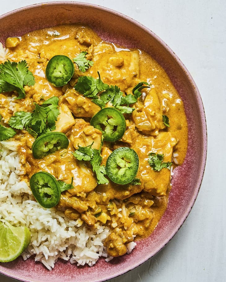 Coconut chicken curry over white rice, with sliced green hot peppers, cilantro, and a lime wedge, in a pink bowl