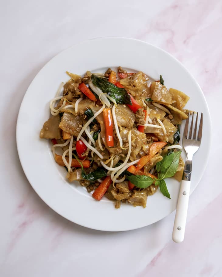 Drunken Noodles (Pad Kee Mao) is a favorite Thai dish made with rice noodles and Thai basil, often eaten in Thailand on late nights after drinking) on a white plate with a fork