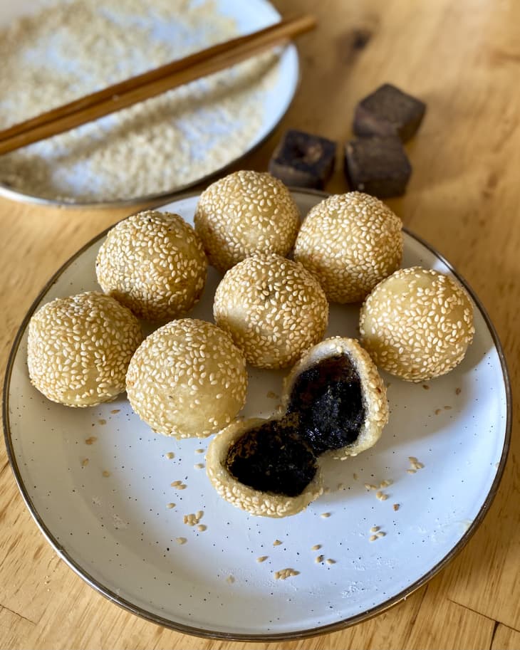 A plate with sesame balls (made with a sticky rice flour dough, filled with a sweet paste, rolled in sesame seeds, and fried until crispy on the outside) with another empty plate in the background with chopsticks on it