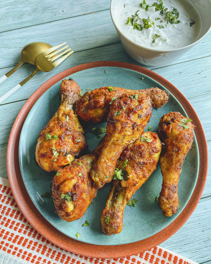 air fryer chicken drumsticks on a turquoise plate, with a dipping sauce and fork and knife on the side