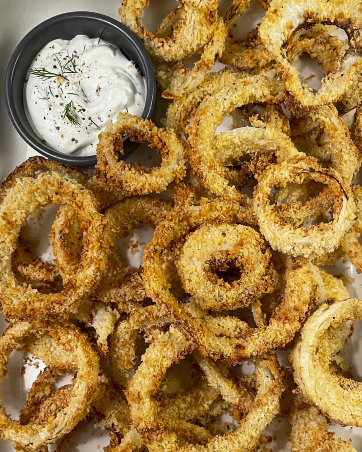 onion rings made in an air fryer, laid out with a small black ramekin with creamy white dipping sauce