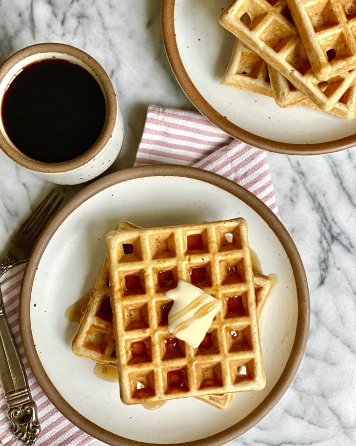 A  rectangular waffle on a round plate, with a pat of butter, a cup of coffee, seen from above